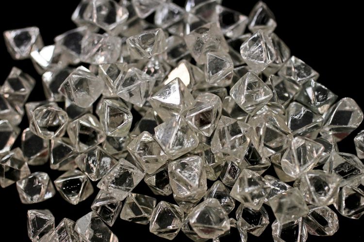 Eine Ansammlung von unbearbeiteten Diamanten mit natürlicher, kristalliner Struktur auf schwarzem Hintergrund.