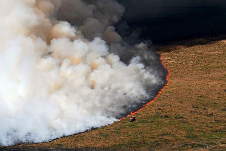 Luftaufnahme eines Feldbrandes in der Nähe von Ares, Südwestfrankreich, mit dichtem Rauch. Ein Feuerwehrfahrzeug und Einsatzkräfte sind am Rand des brennenden Feldes im Einsatz, aufgenommen am 28. Juli 2026.