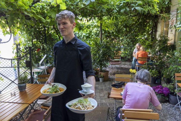Ein Kellner bedient Menschen in einem Gastgarten.