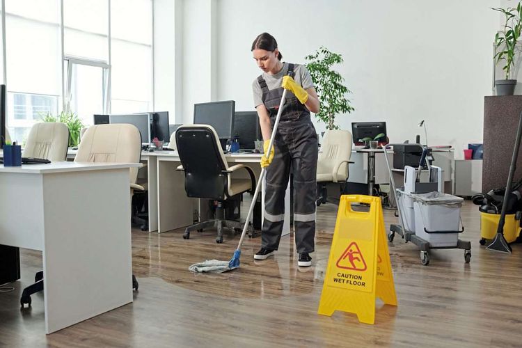 Eine junge Frau putzt einen Büroraum ohne Anwesende