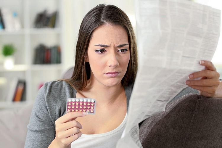 Frau liest skeptisch die Packungsbeilage der Anti-Baby-Pille