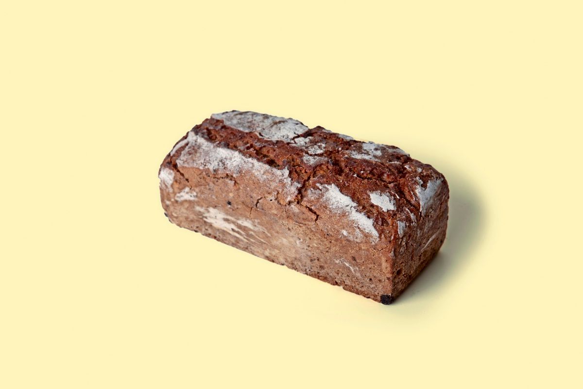 Ein Laib Roggenbrot mit einer dunklen, rustikalen Kruste und leicht bemehlter Oberfläche, präsentiert auf einem hellgelben Hintergrund.