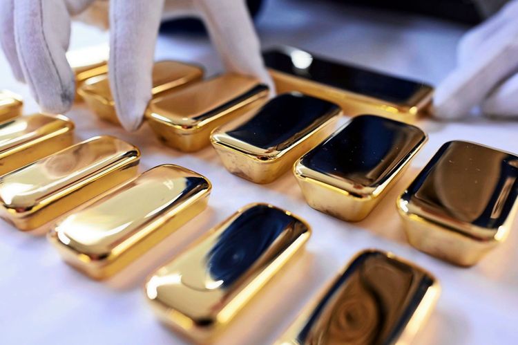 Weiße Handschuhe präsentieren glänzende, frisch gegossene Goldbarren mit einem Feingoldgehalt von 99,99 %. Die Barren sind in drei Reihen angeordnet: oben 1 Kilogramm, in der Mitte 500 Gramm und unten 250 Gramm.