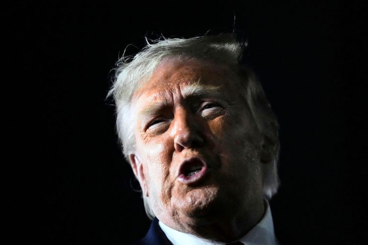 Ein Mann mit blondem Haar spricht energisch, sein Gesicht wird von einer einzelnen Lichtquelle beleuchtet, während der Hintergrund dunkel bleibt.