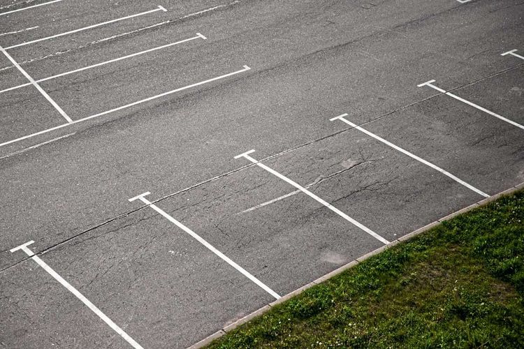 Rechts unten im Bild eine Wiese, den restlichen Teil des Bildes machen leere Parkplätze aus