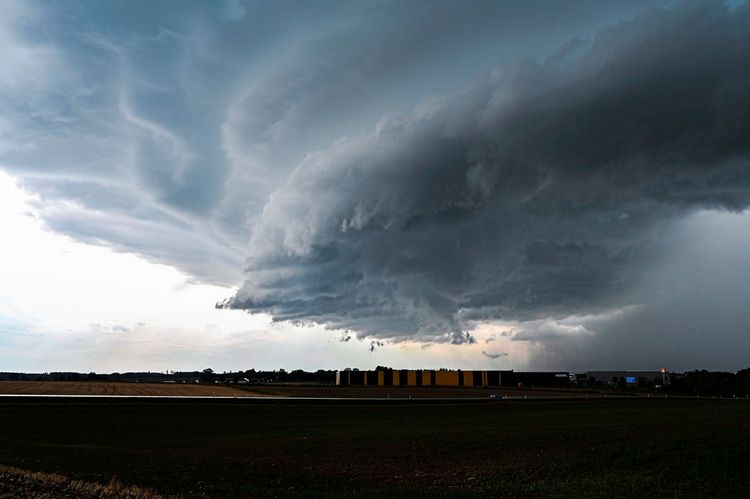 Eine mächtige Gewitterzelle mit dunklen, dramatischen Wolken zieht am Donnerstagnachmittag über Odelzhausen im Landkreis Dachau. Im Vordergrund ist eine landwirtschaftliche Fläche und im Hintergrund Gebäude zu sehen. Der Himmel wird von der markanten Gewitterfront dominiert.