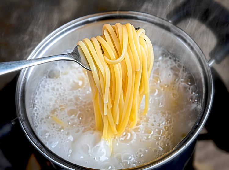 Linguini, die mit einer Gabel aus dem kochenden Wasser geholt werden