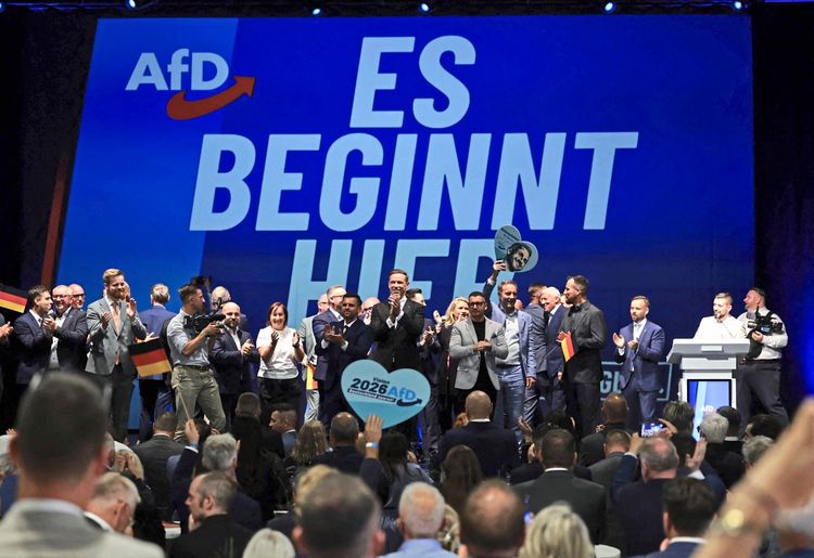 Eine Gruppe von Menschen, darunter Mitglieder und Unterstützer der AfD, feiert auf einer Bühne bei einer Wahlveranstaltung in Magdeburg nach der Bekanntgabe erster Hochrechnungen zu den Landtagswahlen in Sachsen-Anhalt. Im Hintergrund ist ein großer Bildschirm mit der Aufschrift 