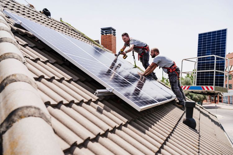 Zwei Arbeiter montieren eine Photovoltaik-Anlage auf einem Dach.