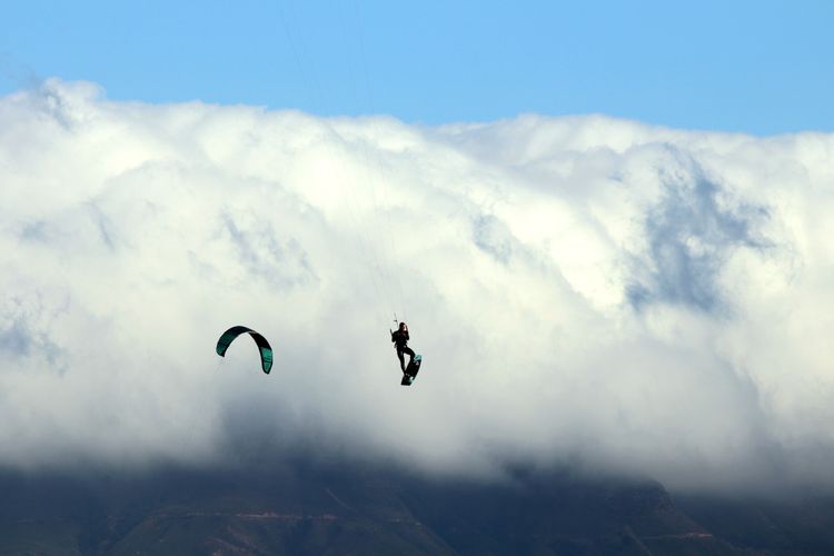 Kitesurfer am Bloubergstrand in Südafrika. Im Hintergrund in den Wolken versteckt sich der Tafelberg. 