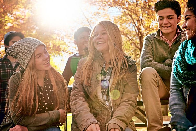 Eine Gruppe junger Menschen sitzt im Freien bei Sonnenschein beisammen
