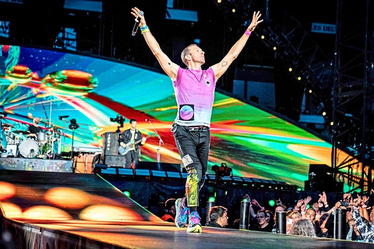 Coldplay-Sänger Chris Martin bei einem Live-Konzert auf einer Bühne, die in buntes Licht getaucht ist