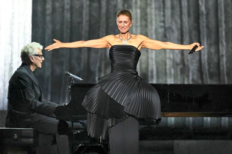 Kanadische Sängerin in einem eleganten schwarzen Kleid mit ausgestreckten Armen auf einer Bühne. Im Hintergrund ein Pianist an einem Flügel. Bühne in gedämpfter Beleuchtung.