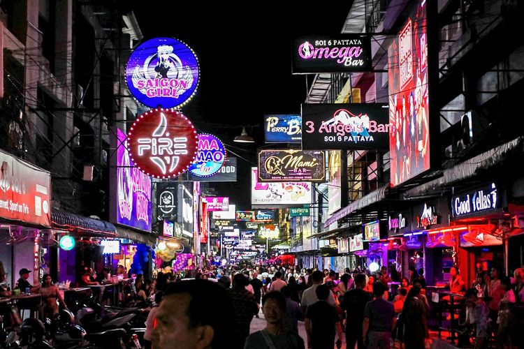 Straße in Pattaya City, Thailand, bei Nacht. Menschen flanieren entlang von Bars und Unterhaltungslokalen mit leuchtenden Neonreklamen.