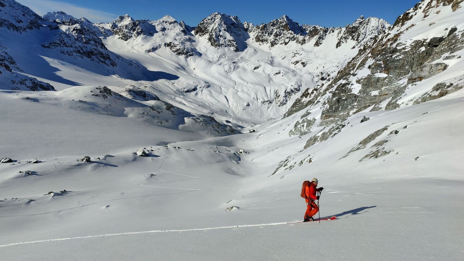 Ein Mann in Skiausrüstung marschiert durch den Tiefschnee in hochalpinem Gebiet