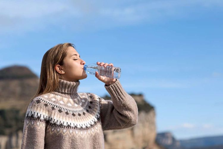 Frau in Pullover trinkt Wasser aus Plastikflasche