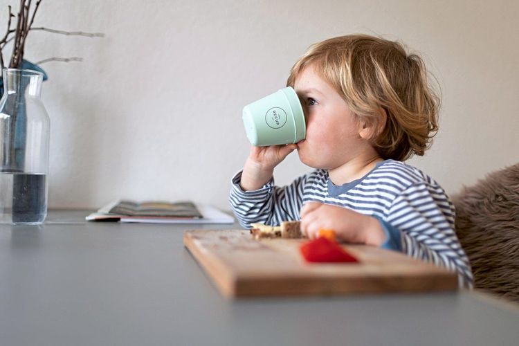 Ein Kind trinkt aus der Tasse und isst ein Butterbrot.