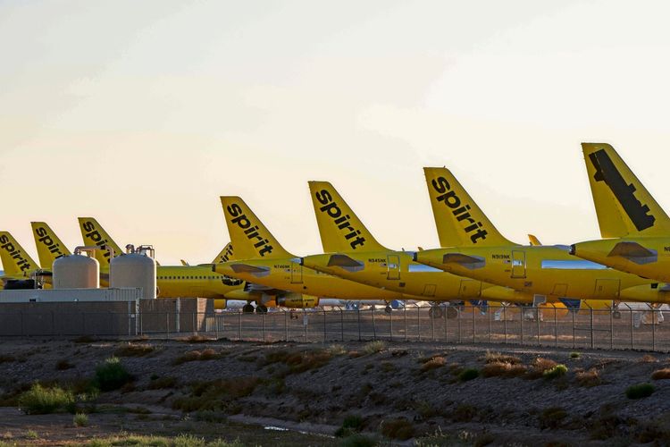 Mehrere gelbe Flugzeuge von Spirit Airlines stehen geparkt auf dem Flughafengelände, umgeben von Zaun und Wassertanks, in einer trockenen, wüstenartigen Umgebung bei Sonnenuntergang.