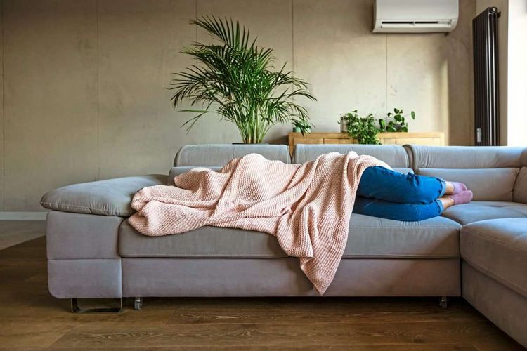 Frau liegt auf dem Sofa, der Oberkörper inklusive Kopf ist bedeckt mit einer hellrosa Decke