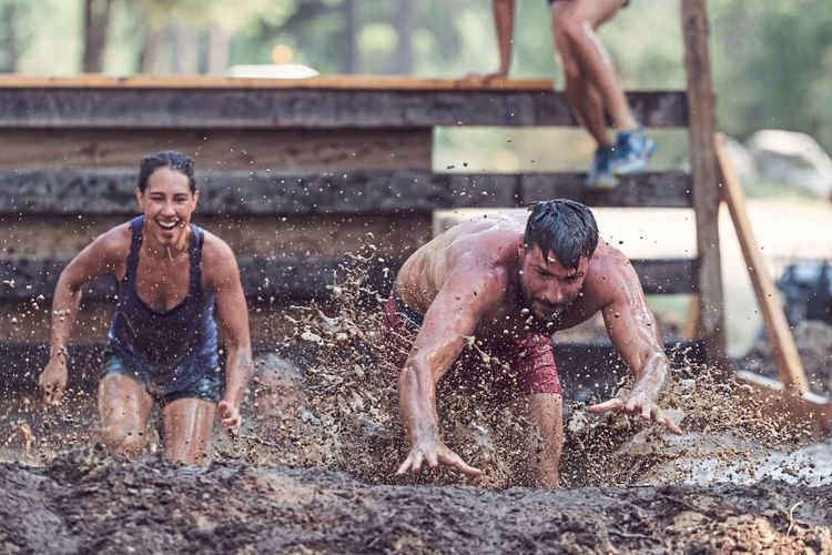 Junge Frau und junger Mann laufen bei Dirtrun durch schlammiges Wasser.