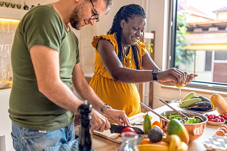 Junges Paar, sie ist schwanger, kocht mit viel Gemüse