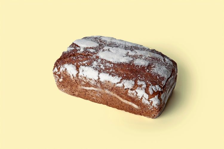 Ein Laib Roggenbrot mit bemehlter Kruste auf hellem, gelbem Hintergrund.