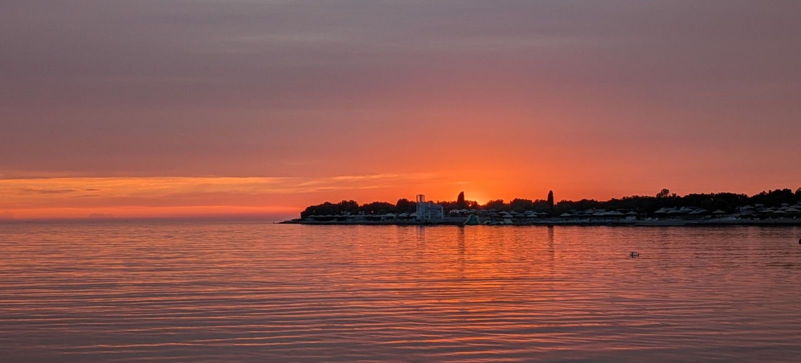 Rot leuchten Himmel und Meer, während die Sonne am Horizont hinter der Silhouette einer Stadt versinkt.