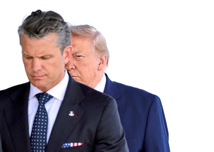 Zwei Männer in Anzügen sind abgebildet. Der Mann im Vordergrund ist unscharf, während der Mann im Hintergrund teilweise sichtbar ist, sein Gesicht schaut hinter dem anderen hervor. Der Hintergrund ist weiß und neutral.