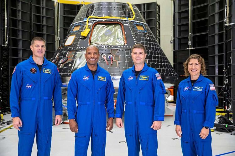 Drei Astronauten und eine Astronautin in blauen Anzügen vor einer ungefähr kegelförmigen schwarzen Kapsel