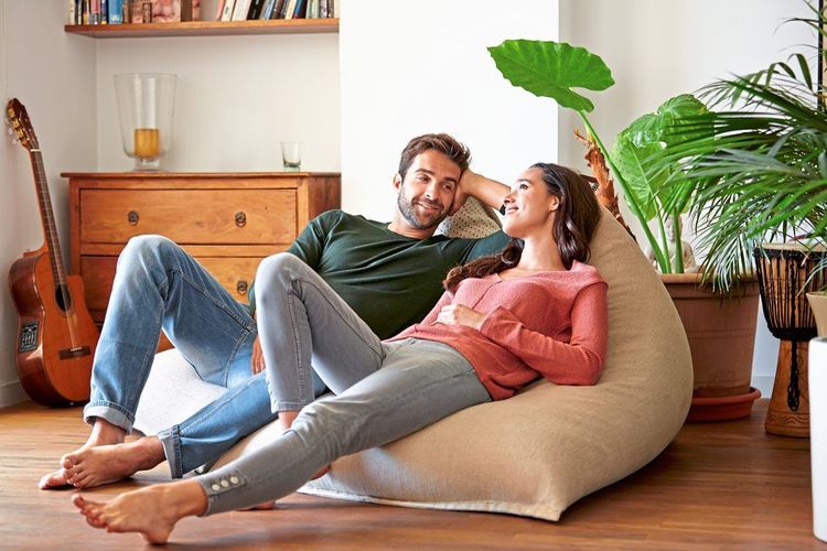 Ein Mann und eine Frau liegen lächelnd und plaudernd einander zugewandt auf einem Sitzsack in einer heimelig wirkenden Wohnung