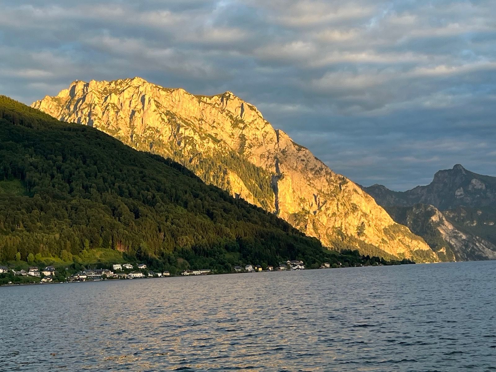 Ein Berg wird von der Sonne beschienen, davor ein See.