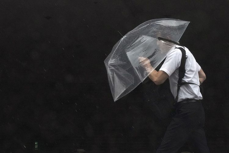 Mann mit Regenschirm im Taifun, Japan