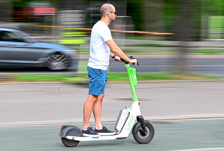 Mann fährt einen Lime-E-Scooter auf einem Fahrradstreifen.