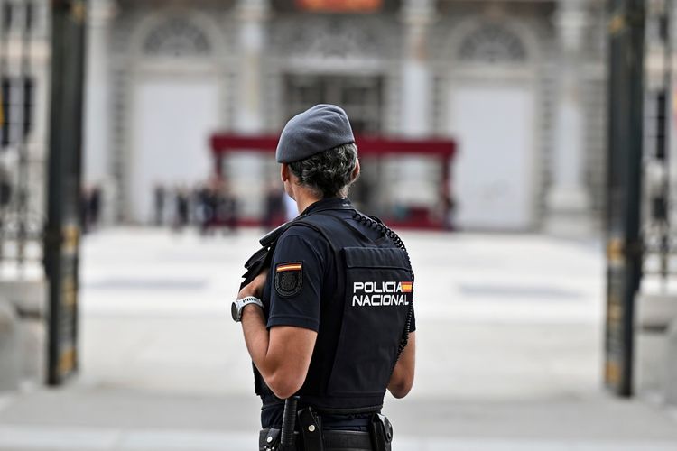 Ein Polizist der spanischen Nationalpolizei steht Wache in der Nähe des Königspalastes in Madrid, Spanien. Im Hintergrund ist der Palast mit unscharfen Details zu sehen.