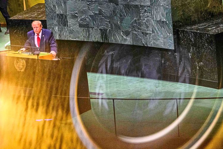 Ein Mann steht an einem Rednerpult während einer Versammlung in den Vereinten Nationen. Das Bild wurde durch eine Reflexion auf einem mobilgerät aufgenommen, wodurch kreisförmige Lichtspuren sichtbar sind.