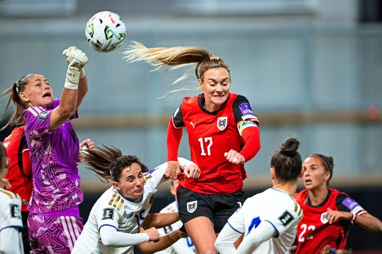 Eine Szene aus einem Frauenfußballspiel zwischen Österreich und Kosovo im Rahmen des Play-off-Rückspiels der WM-Qualifikation am 13. Oktober 2026 in Wien. Eine österreichische Spielerin im roten Trikot springt zum Kopfball, während die kosovarische Torhüterin im lilafarbenen Trikot versucht, den Ball abzuwehren. Weitere Spielerinnen sind im Hintergrund zu sehen.