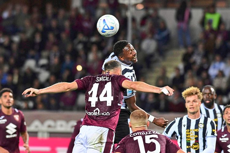 Ein Fußballspiel der Serie A zwischen Torino und Udinese. Spieler von beiden Mannschaften springen nach einem Kopfball. Im Vordergrund trägt ein Spieler von Torino die Nummer 44, während ein Spieler von Udinese den Ball mit dem Kopf trifft. Im Hintergrund sind weitere Spieler und Zuschauer zu sehen.