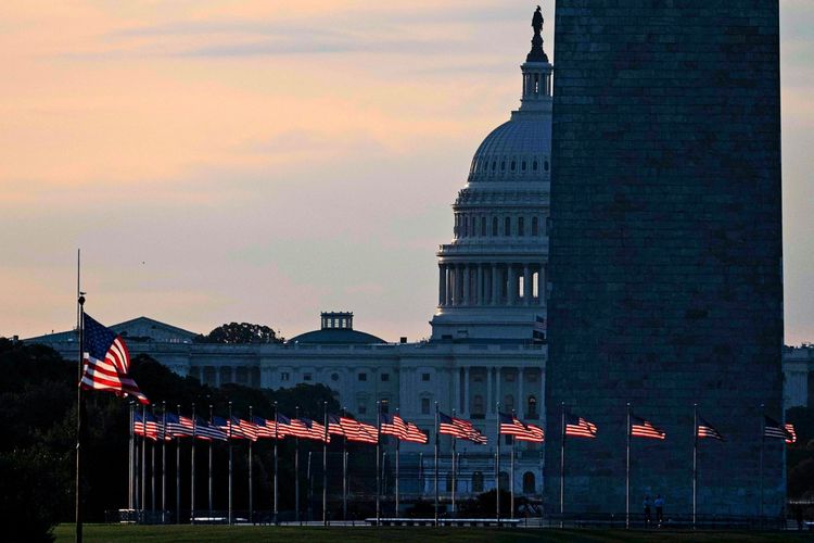 Blick auf die Kuppel des US-Kapitols und das Washington Monument bei Sonnenaufgang, umgeben von wehenden US-Flaggen auf der National Mall in Washington, D.C.