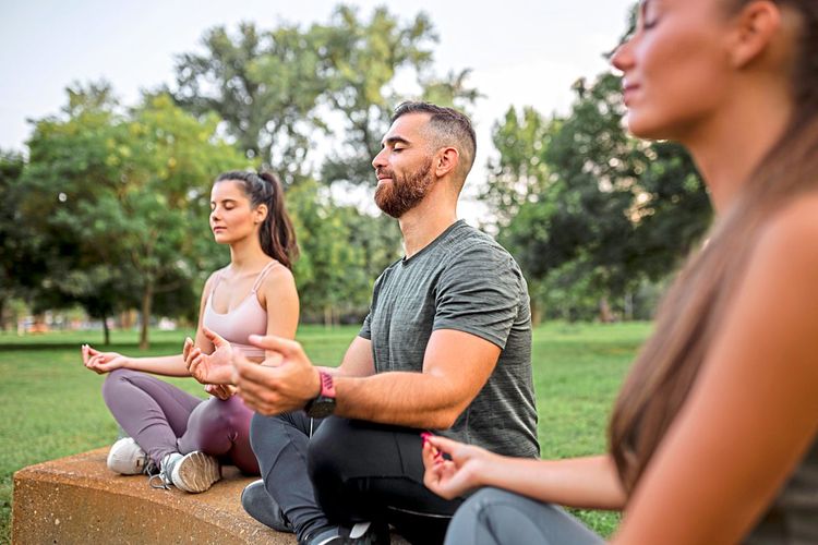 Drei junge Menschen sitzen auf einer Wiese und meditieren
