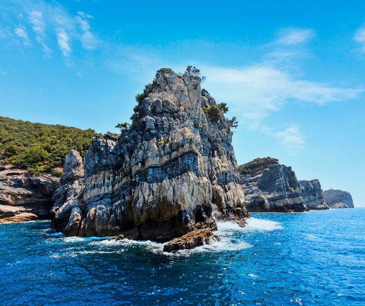 Felsige Küste der Insel Palmaria im Golf der Poeten nahe Portovenere, Italien, mit türkisblauem Meer, steilen Klippen und einem klaren Himmel im Hintergrund.