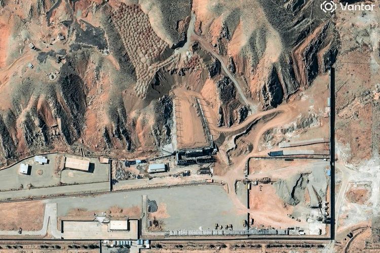 Satellitenbild einer Anlage in einem hügeligen, kargen Gelände, umgeben von Straßen und Gebäuden. In der Mitte ist eine größere Struktur zu sehen, die sich teilweise in die Landschaft integriert. Die Anlage ist von Zäunen oder Mauern begrenzt.