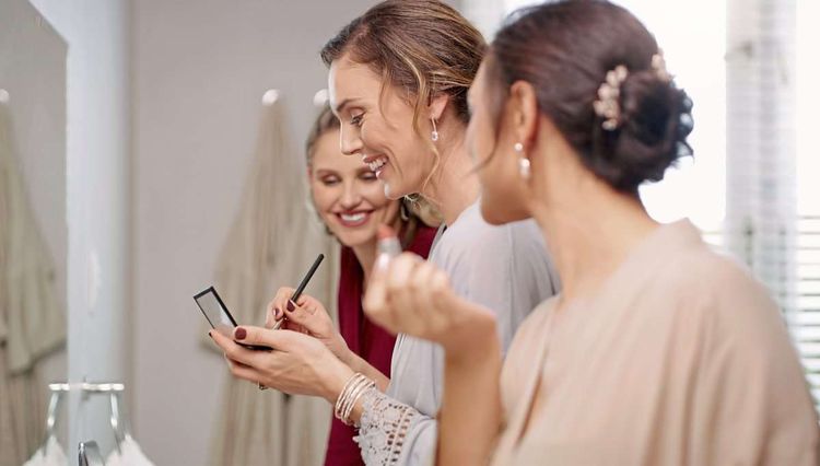 Group of happy, beautiful and elegant bridesmaid women getting ready, applying makeup and dressing in the bathroom for a wedding. Modern young and pretty ladies putting on cosmetics in a mirror; Schminken,