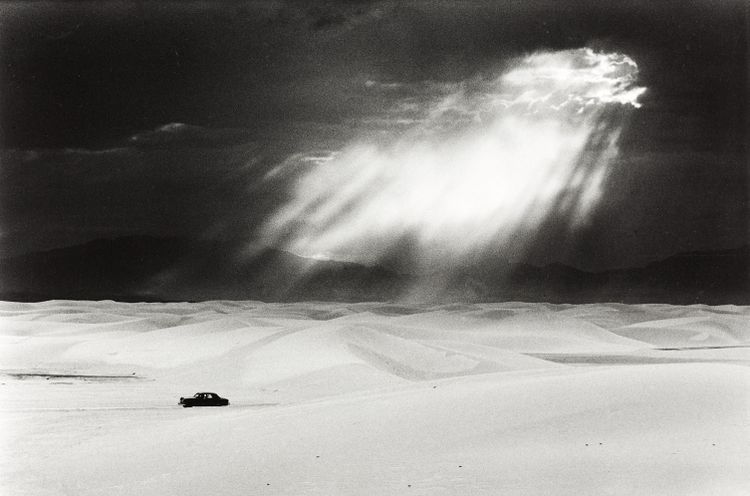 White Sands, New Mexico 1952: Auch für dieses Werk des österreichischen Magnum-Fotografen Ernst Haas (1921-1986) lieferte eine pittoreske Wüstenlandschaft das Setting. Helle Gipsdünen, ein dunkles Firmament und die Sonne, die durch die Wolkendecke bricht – aufgenommen in White Sands, New Mexico.