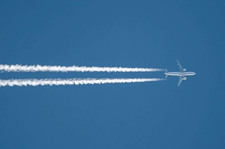 Ein Flugzeug zieht vor blauem Himmel einen Kondensstreifen nach sich