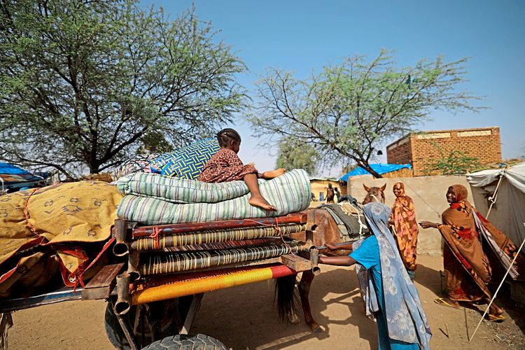 Flüchtlinge aus Darfur rund um ein Pferdefuhrwerk mit Decken und anderen Habseligkeiten.
