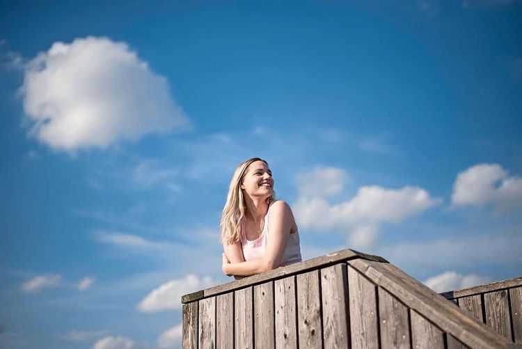 Eine junge Frau steht auf einer Holzterrasse und lacht