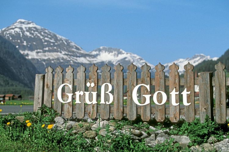 Grüß Gott als Schriftzug an einem Zaun, dahinter Tiroler Berge