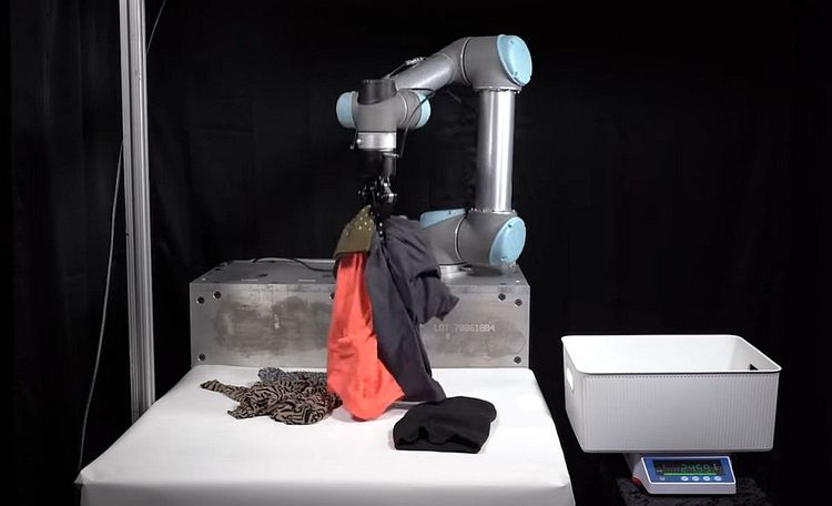 Roboterarm greift mehrere Wäschestücke auf einmal.