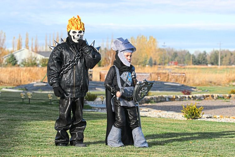 Zwei Kinder in Halloweenkostümen (Skelett und Ritter) laufen über eine Wiese