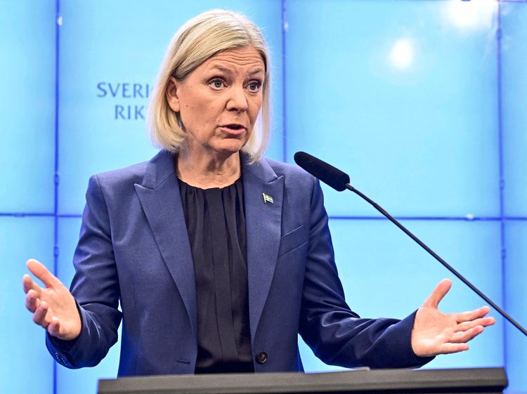 Eine blonde Frau in blauem Blazer hinter einem leuchtend blauen Hintergrund.